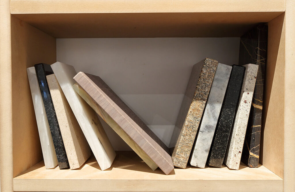 Na zdjęciu widzimy jasną, drewnianą półkę z książkami, które wykonane są z różnych gatunków marmuru.