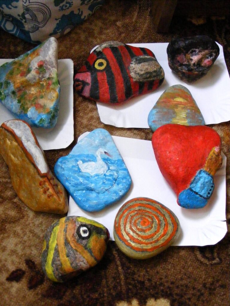 Dziewięć kamieni pomalowanych przez uczestników pleneru. Namalowali pejzaże, ryby, but i łabędzie.