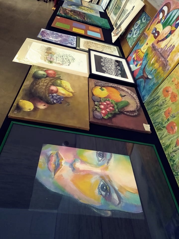 różnokolorowe obrazy ( martwa natura, portret, pejzaż) ułożone na stołach