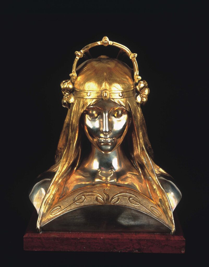 Rzeźba przedstawia głowę dziewczyny w złotej koronie i złotych, długich włosach, swobodnie opadających na srebrne ramiona. Srebrna twarz z zamkniętymi oczami skierowana jest centralnie. Rzeźba osadzona jest na postumencie z ciemno- czerwonego kamienia. Przestrzeń nad kamieniem między ramionami i włosami jest wypełniona łukiem z brązu. i Nnad nim umieszczono dodatkowy ozdobnym łukiem ze złota przypominającym w kształciet otwartej książki.