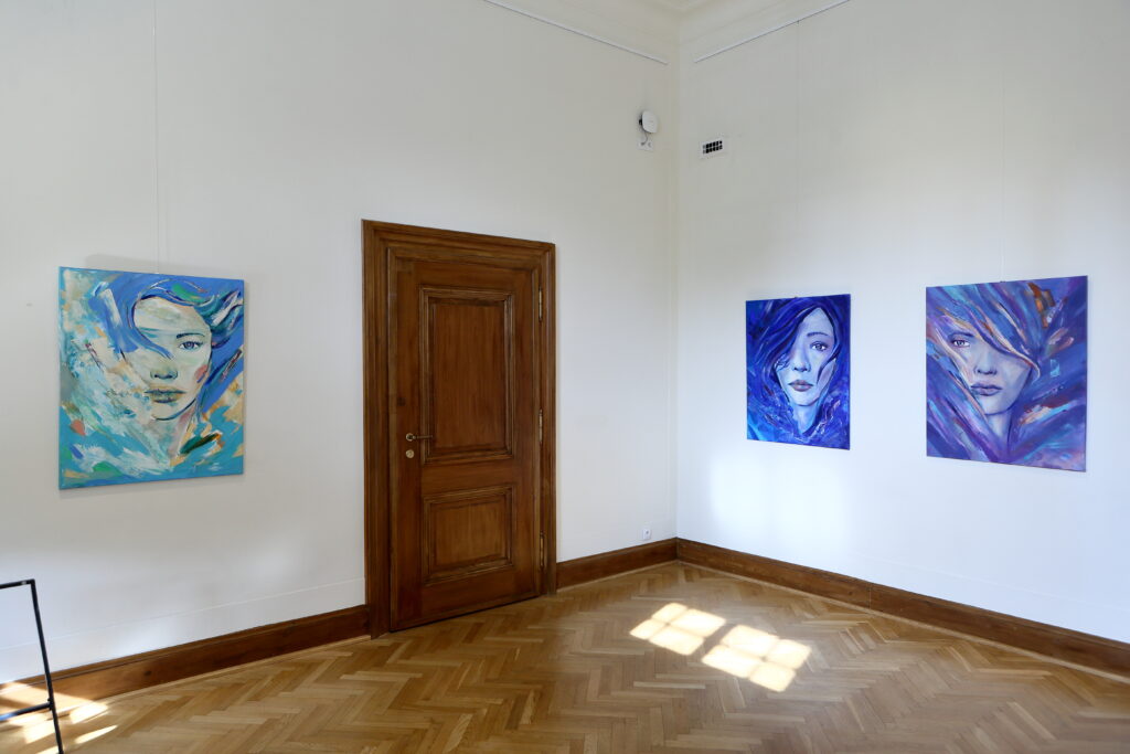Od lewej widoczny portret kobiety w błękicie, następnie zamknięte drzwi do sąsiedniego pomieszczenia. Po prawej stronie umieszczono dwa portrety w kolorze ciemnoniebieskim, wszystkie na płótnie.