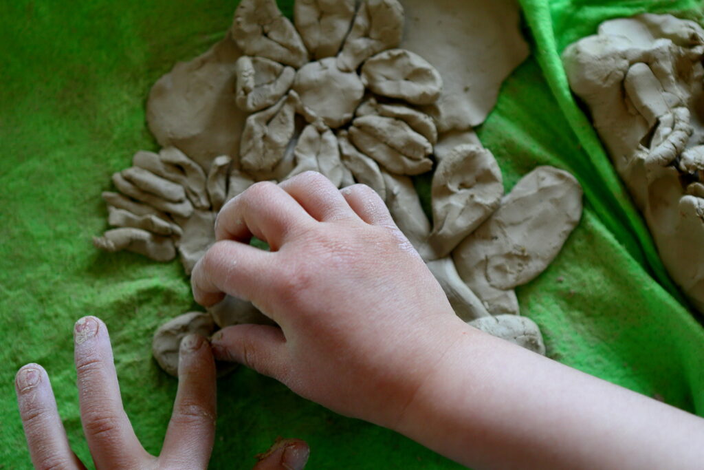 Kadr-zbliżenie. Ręce dziecka lepiącego z gliny kwiatki.