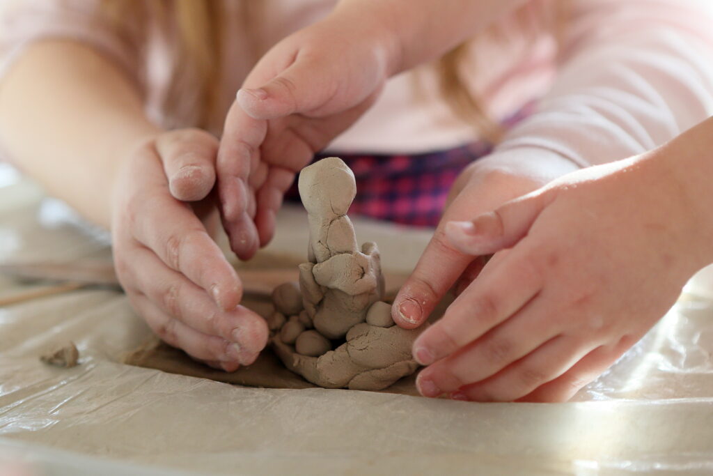 Kadr-zbliżenie. Prowadząca i dziecko okalają swoimi dłońmi figurkę z gliny.