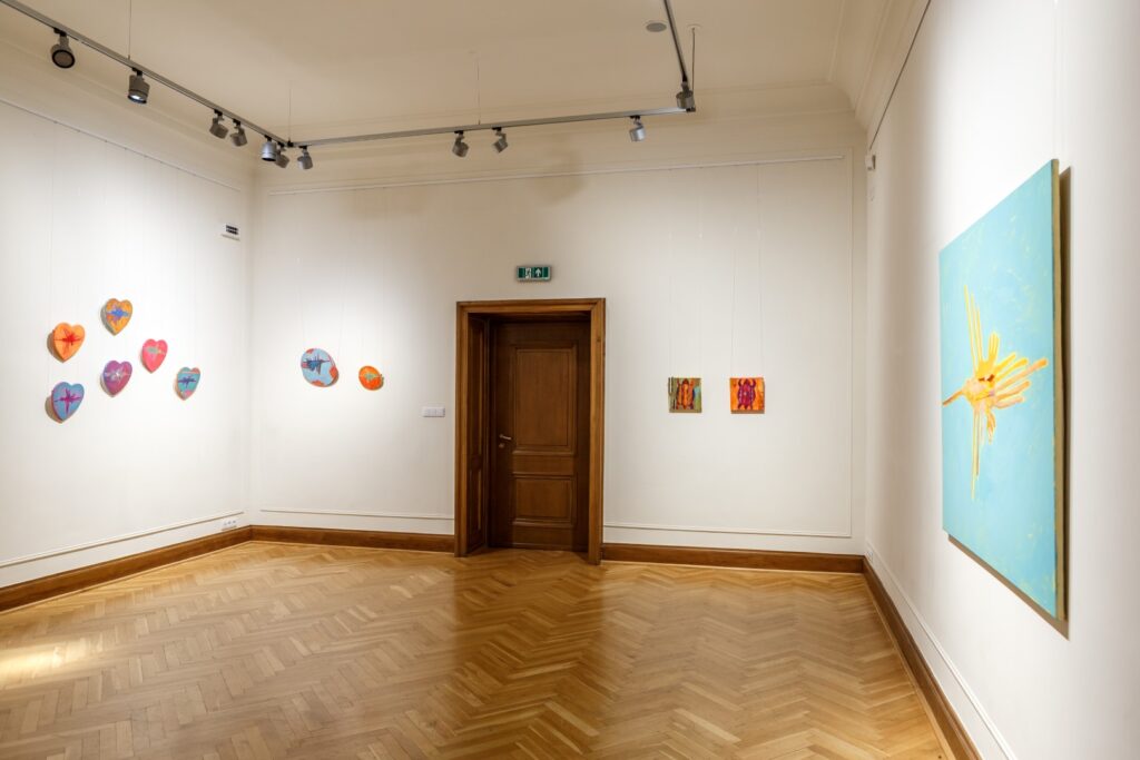 Po prawej stronie duży obraz z motywem żółtego kolibra na błękitnym tle. Na wprost małoformatowe obrazy